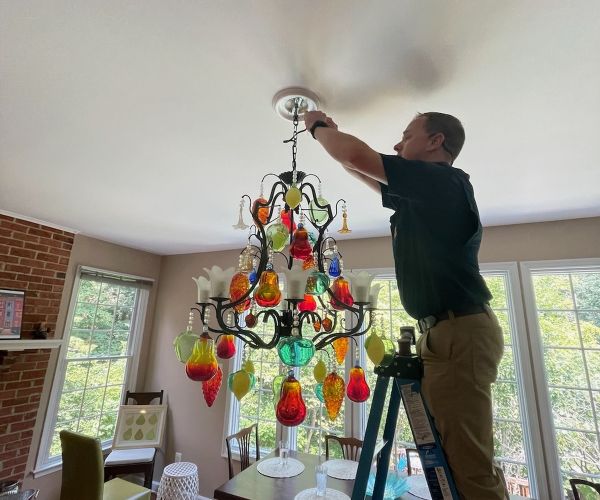 Man Replacing Bulb On Colorful Chandelier In Dining Room