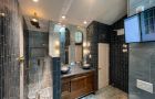 Modern Bathroom With Dark Tiles And Wooden Vanity And Mirrors